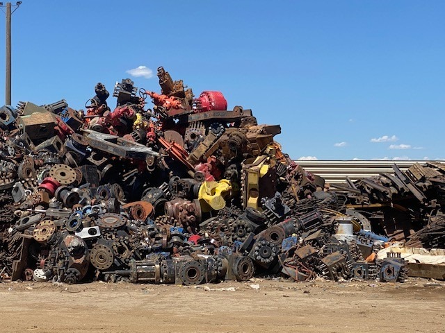 A large heap of discarded machinery and metal parts in a junkyard, highlighting the accumulation of scrap materials against a clear blue sky.