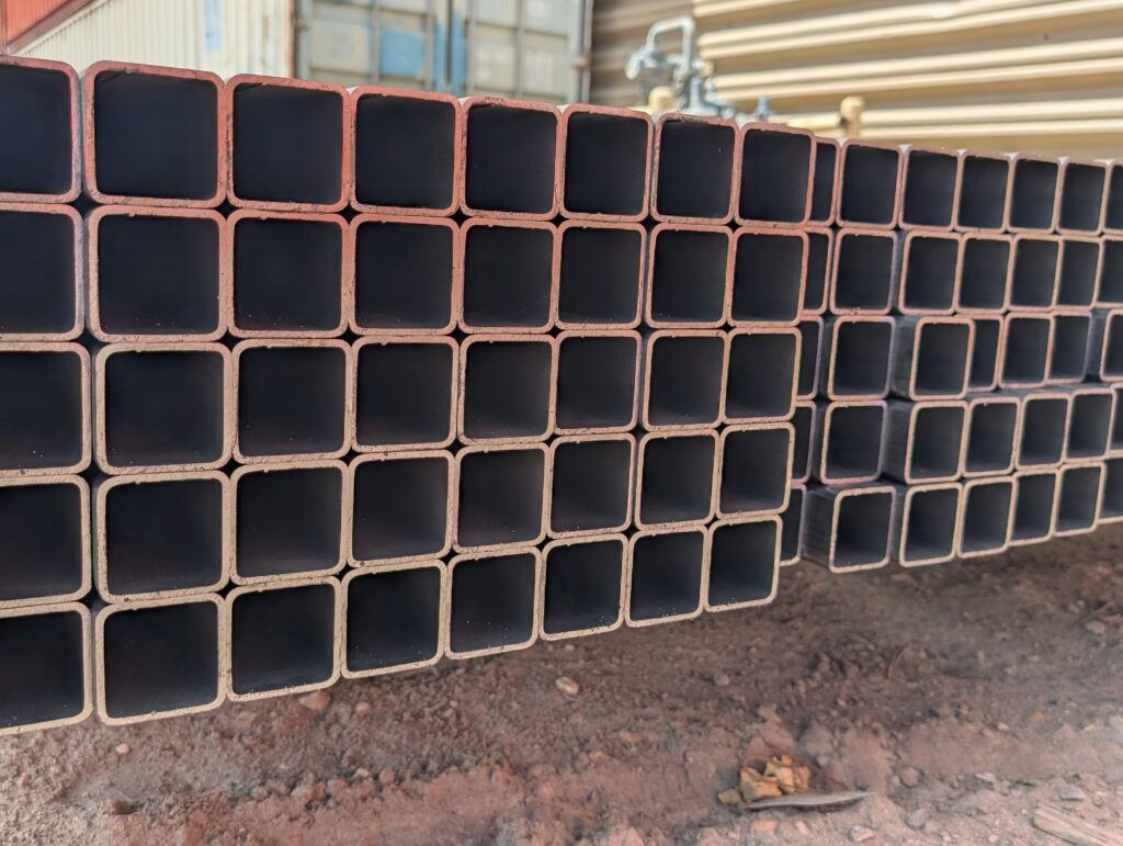 Stacked steel square tubes on a construction site, showcasing their uniformity and industrial application. Ideal for structural projects.
